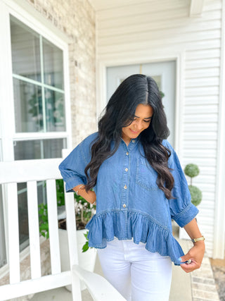 Woman wearing a blue ruffled blouse and white pants on a porch.