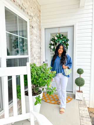Woman standing on a porch with plants and a decorative wreath.